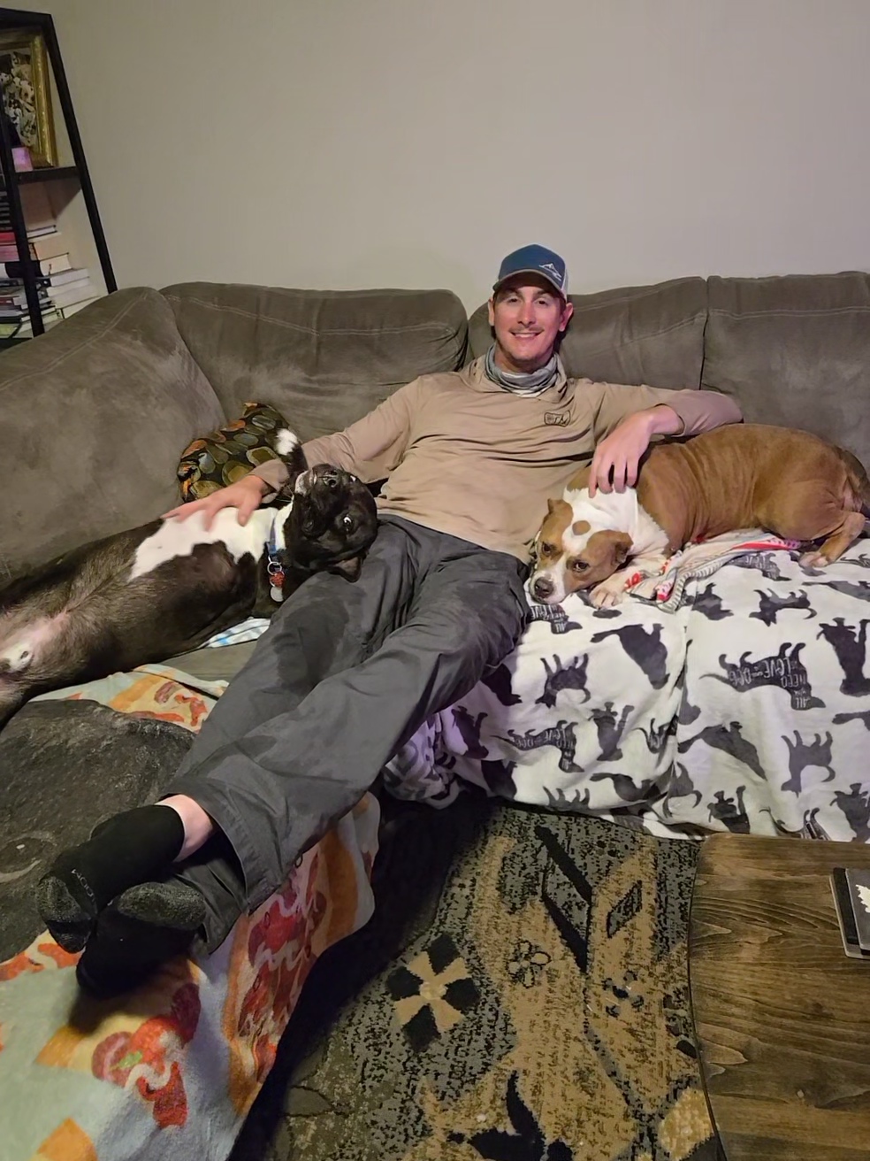 two dogs flank a man relaxing on a couch in a living room